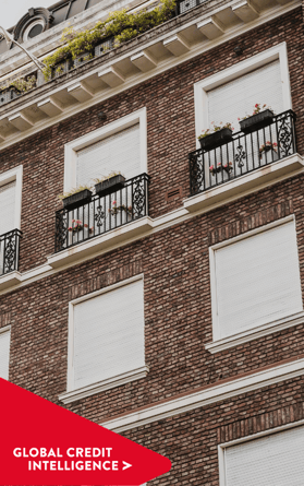 Modern brick commercial building with closed shutters and structured balconies, with a red banner overlay reading 'Global Credit Intelligence,' representing insights into property and credit markets.