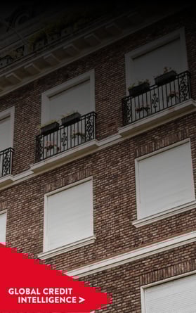 Modern brick commercial building with closed shutters and structured balconies, with a red banner overlay reading 'Global Credit Intelligence,' representing insights into property and credit markets.