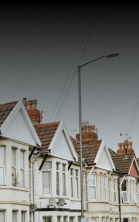 A row of traditional British terraced houses, representing the UK housing market. The image reflects themes of property valuation, mortgage trends, and real estate investment, with an overcast sky setting a neutral backdrop.