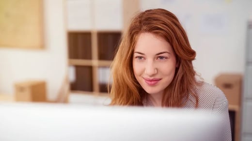 puter smiling as she leans forwards reading text on the screen, view over the monitor