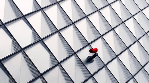 A single red surveillance camera on the tiled wall of an office building