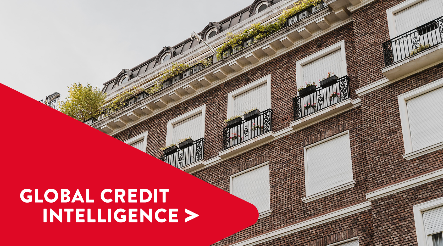 Modern brick commercial building with closed shutters and structured balconies, with a red banner overlay reading 'Global Credit Intelligence,' representing insights into property and credit markets.