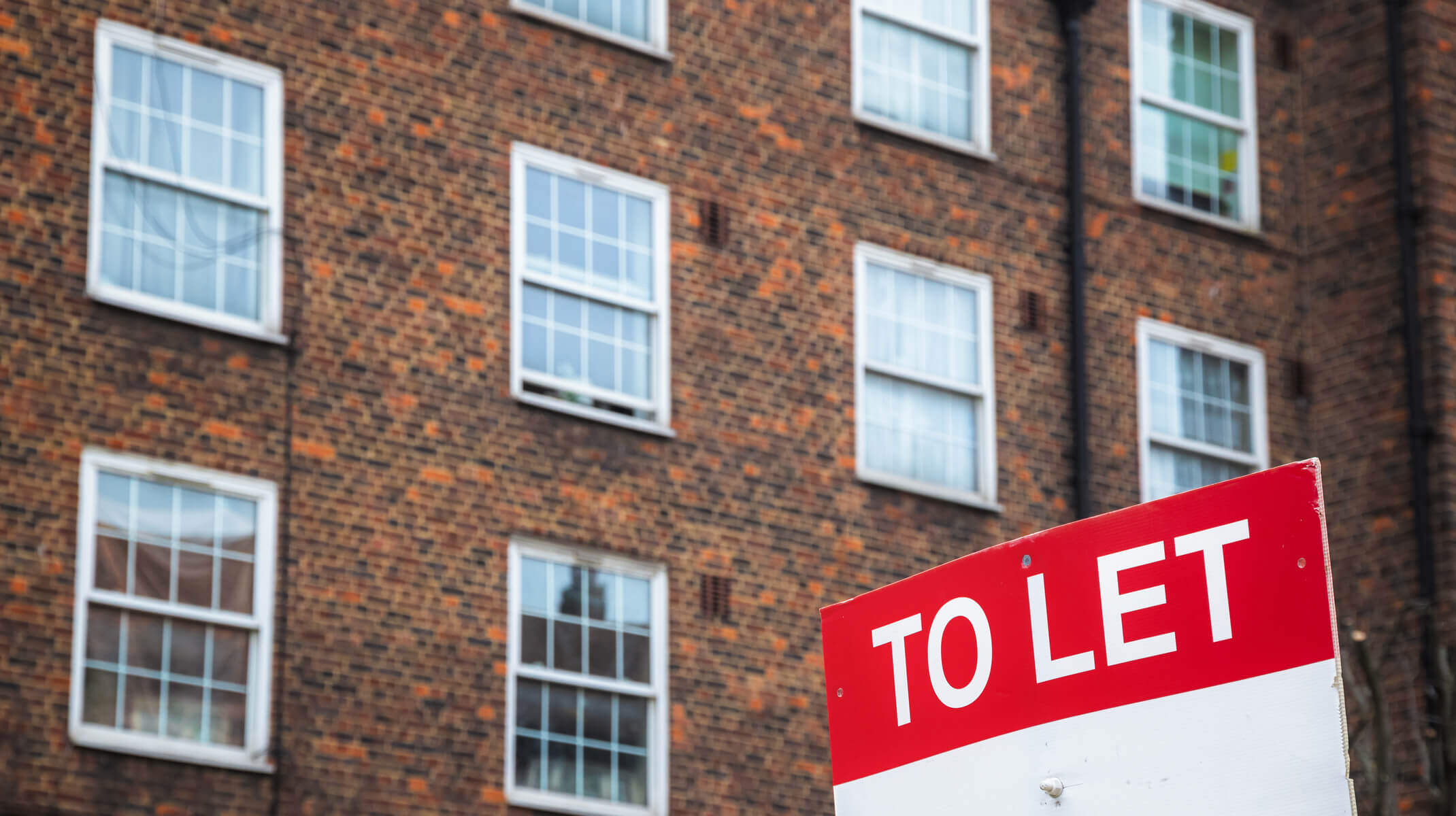 To let sign in front of a dark brown and orange brick building.